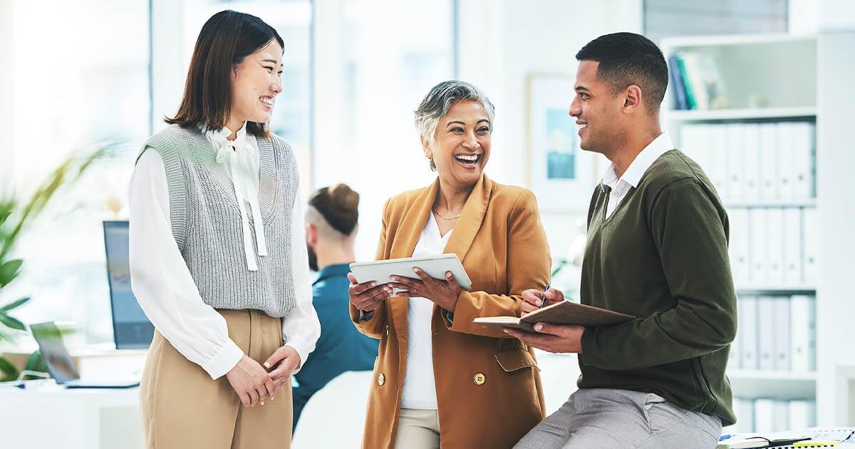 Employees smiling sat down having a talk near a desk