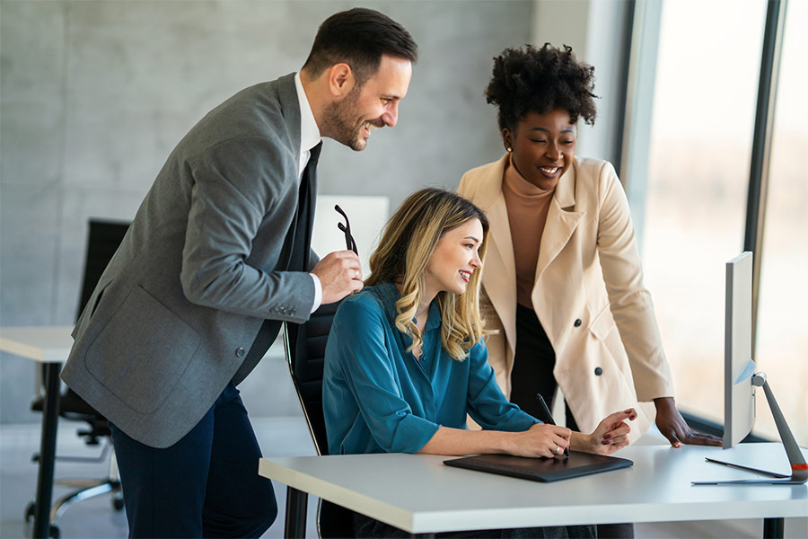 Employee sat at a desk with two other employees next to her, all looking at her screen while she draws on a tablet