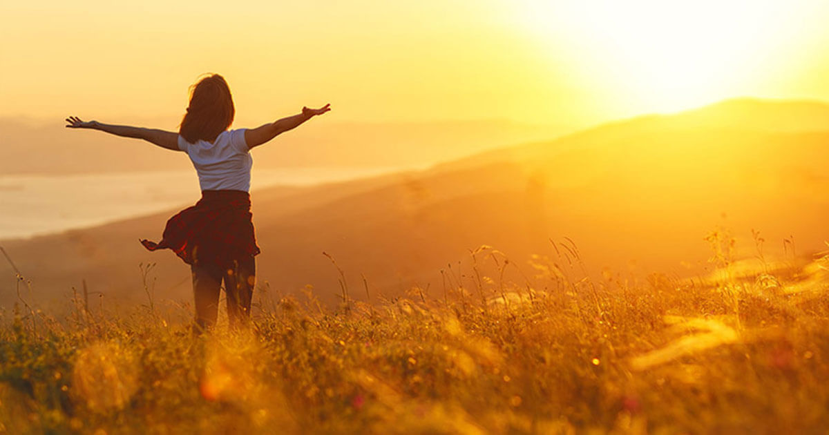 Person facing the sun as it sets over a grassy hill