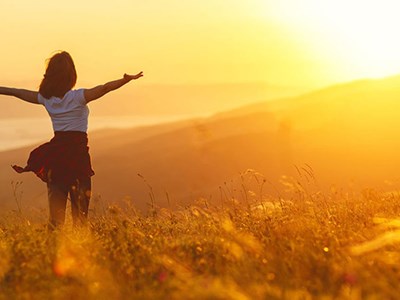 Person facing the sun as it sets over a grassy hill