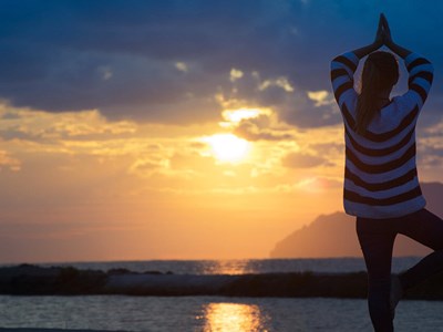 Woman doing yoga on the beach during sunrise.